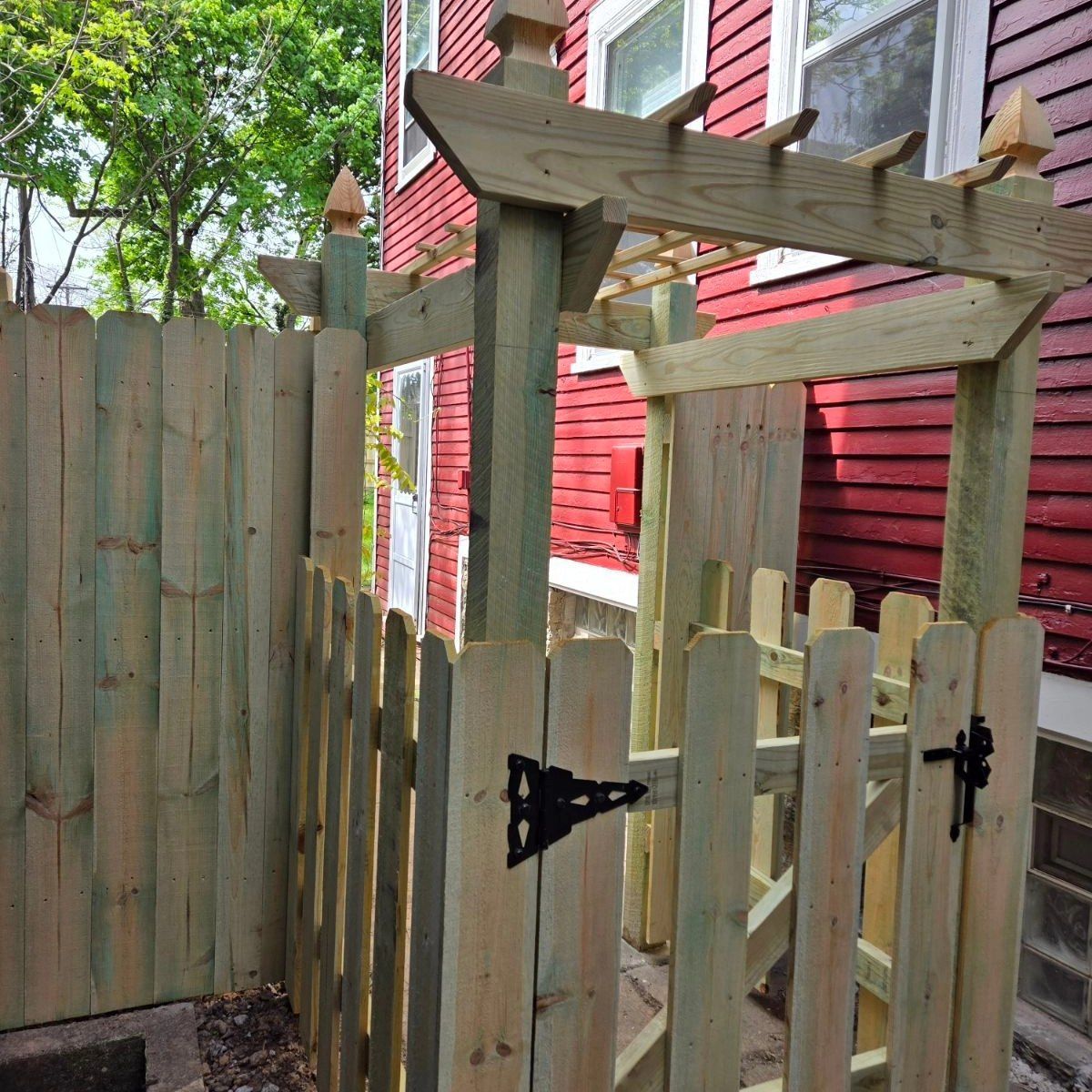 Wooden gate and fence in a backyard beside a red house with white-trimmed windows.