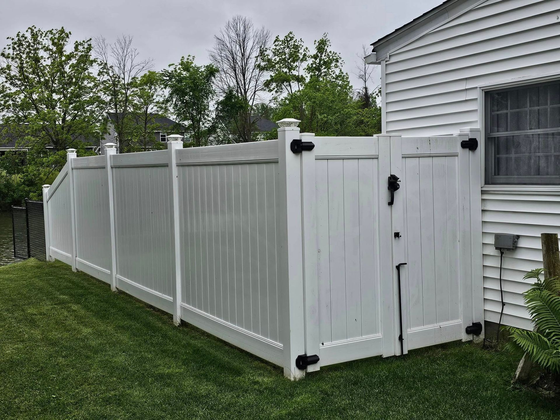 White vinyl fence with a matching gate beside a house in a grassy yard