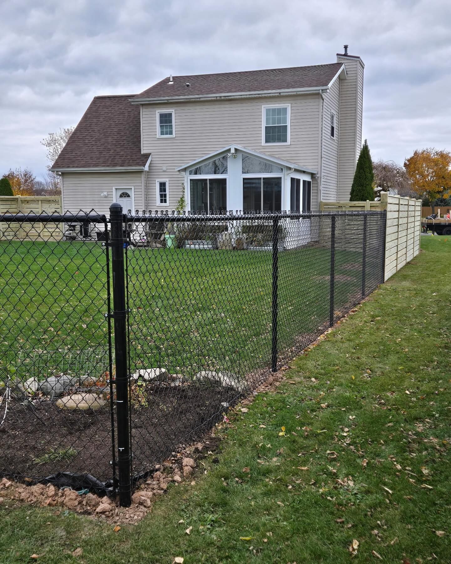 Two-story beige house behind black chain-link fence with grassy yard and patio doors