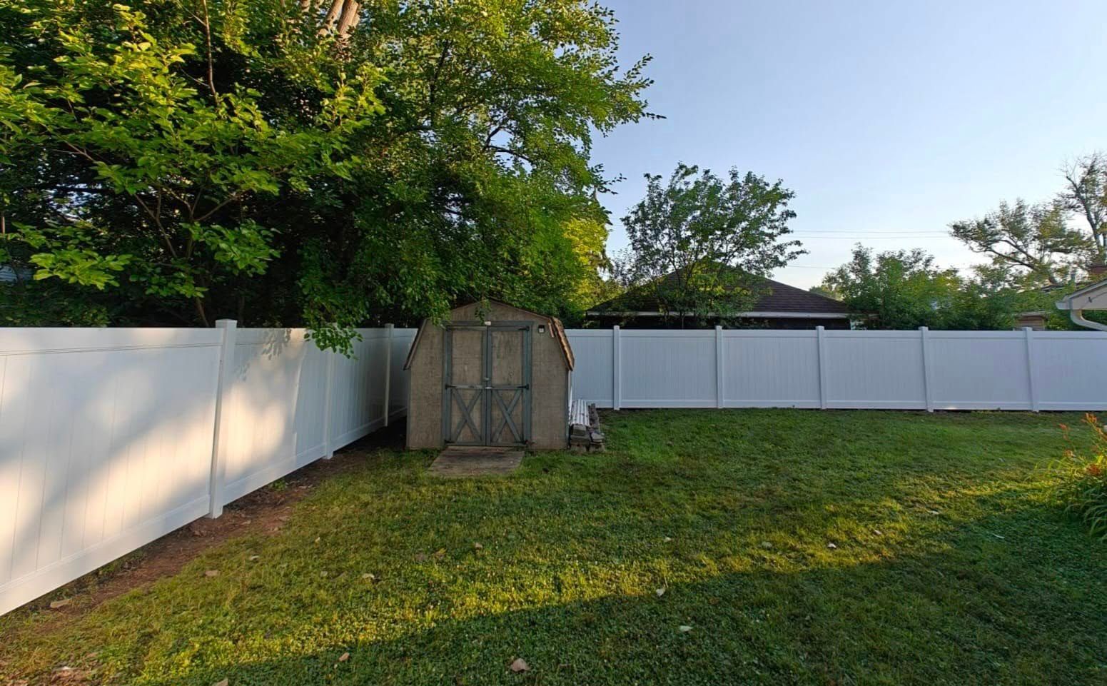 Backyard with white fence, wooden gate, and trees in warm evening light