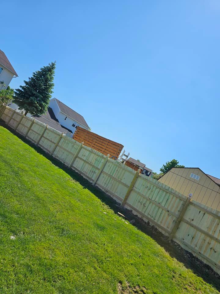 Tilted view of a sunny backyard with green lawn, wooden fence, and suburban houses under a blue sky