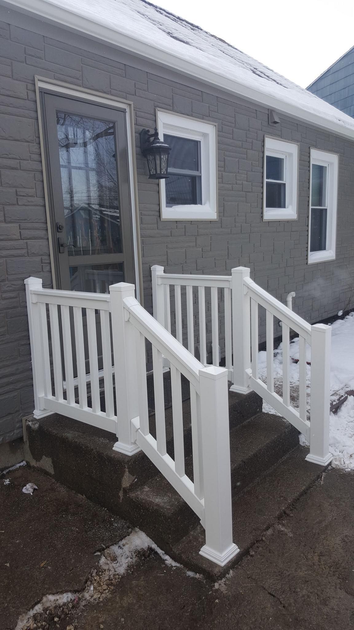 Gray house entrance with white ramp, railings, and steps in snowy weather