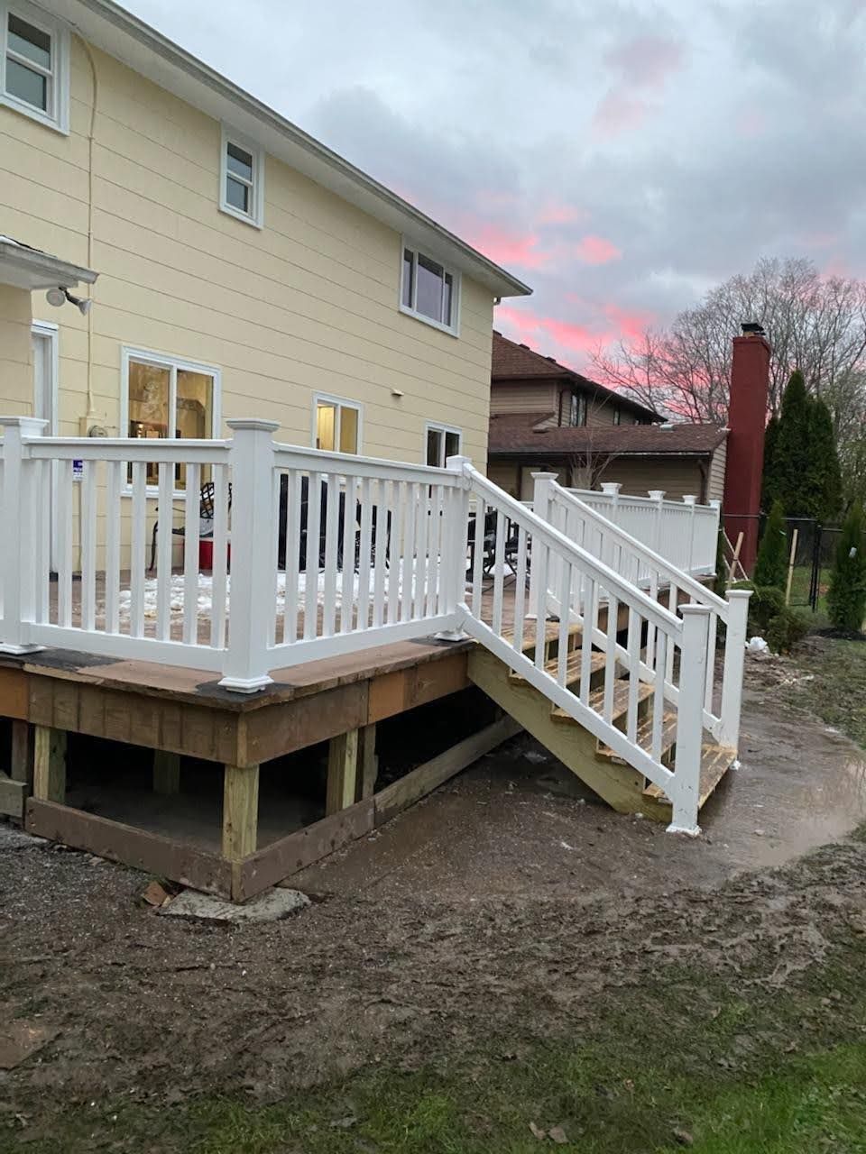 House with white deck and stairs on a dirt yard at dusk