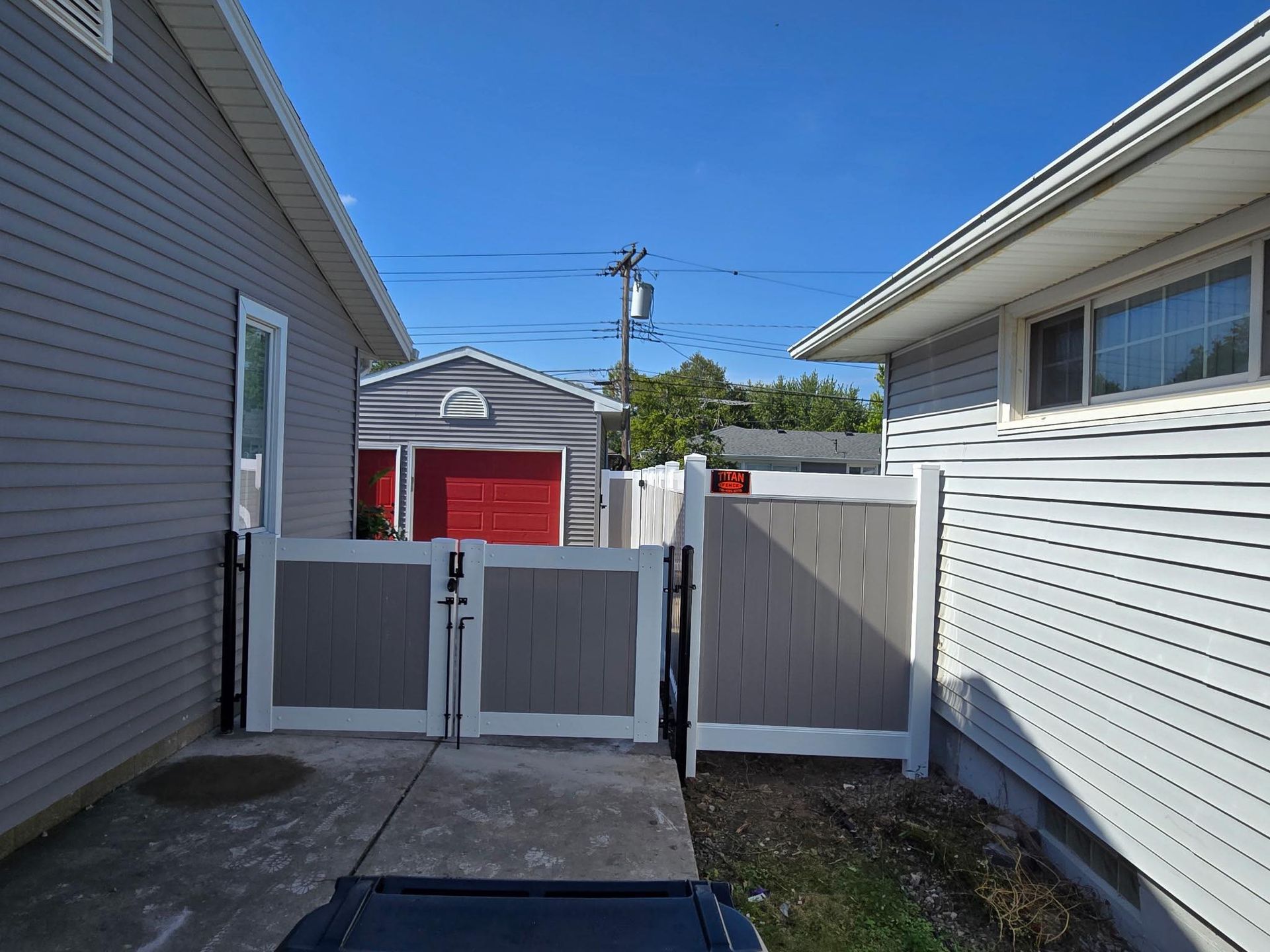 Narrow side yard with white fence gates between two houses, leading to a red garage in the distance.