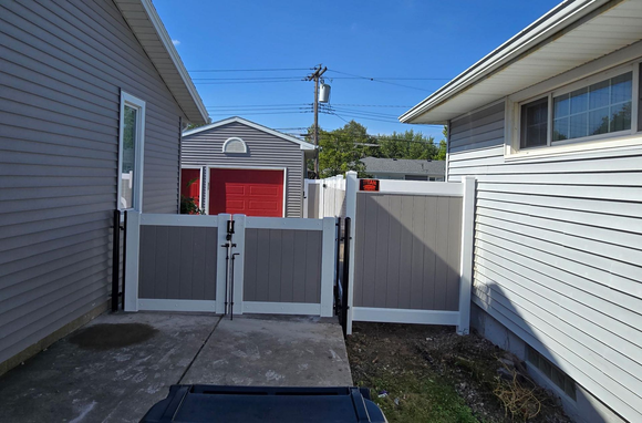 Narrow side yard with gray fences, concrete walkway, and a red garage in the background