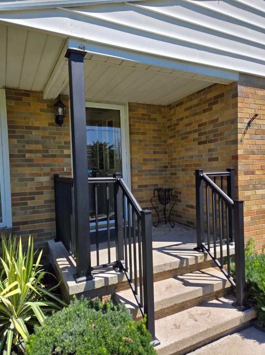 Front porch with brick walls, black railings, steps, and a white awning in front of a brick house