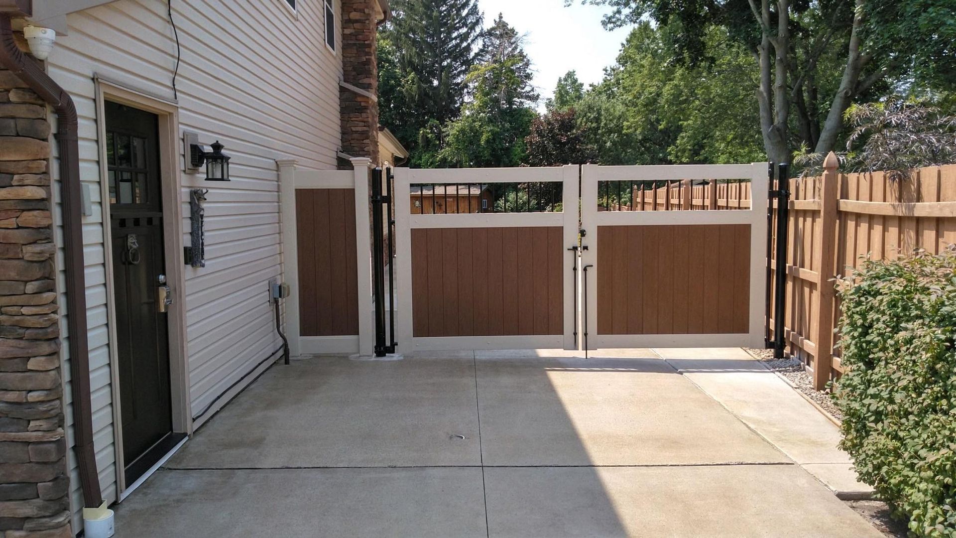 Concrete backyard patio with white-and-brown fence gate and stone house siding on the left