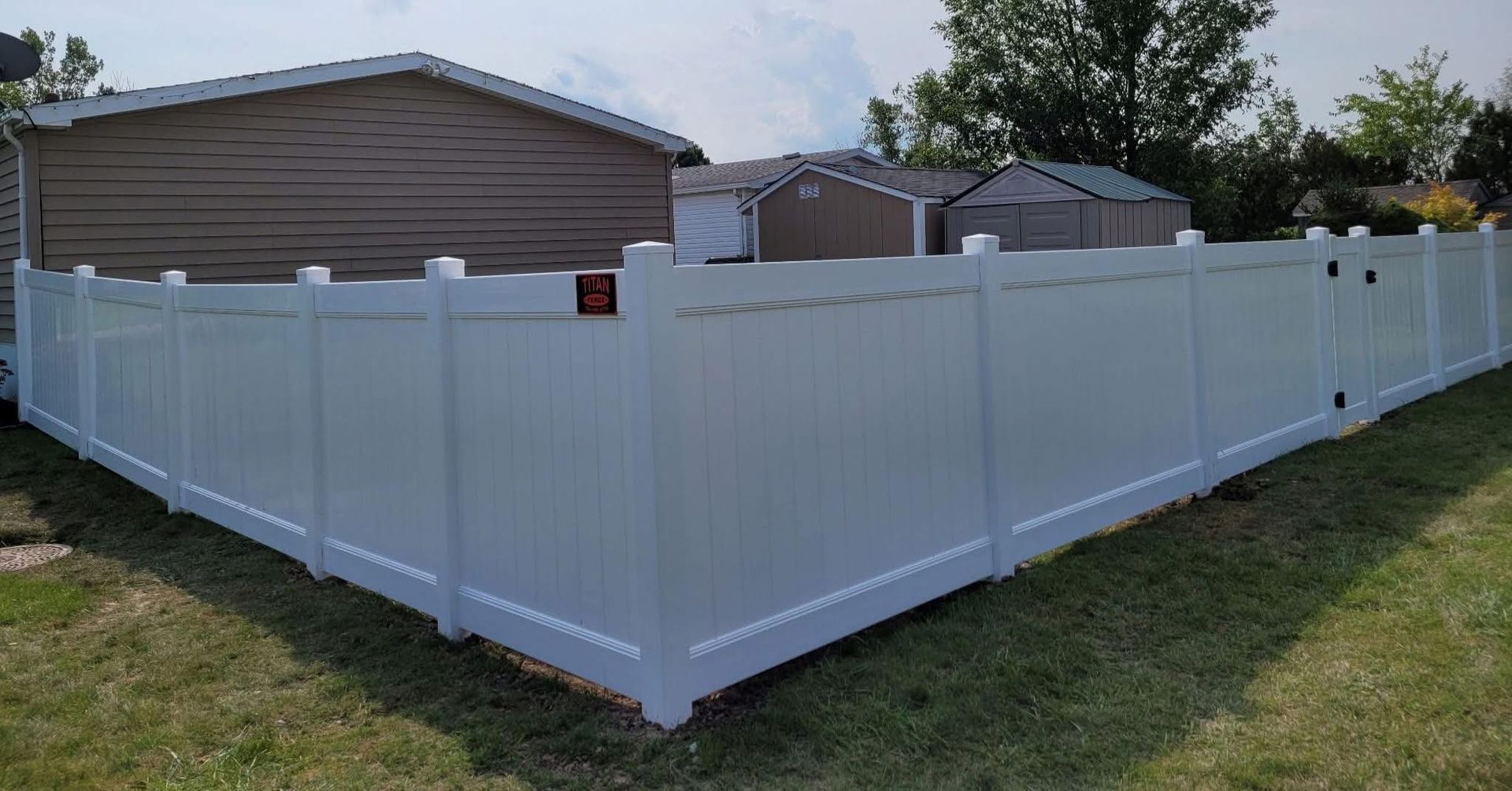 White vinyl privacy fence enclosing a backyard beside a tan house on a grassy lawn