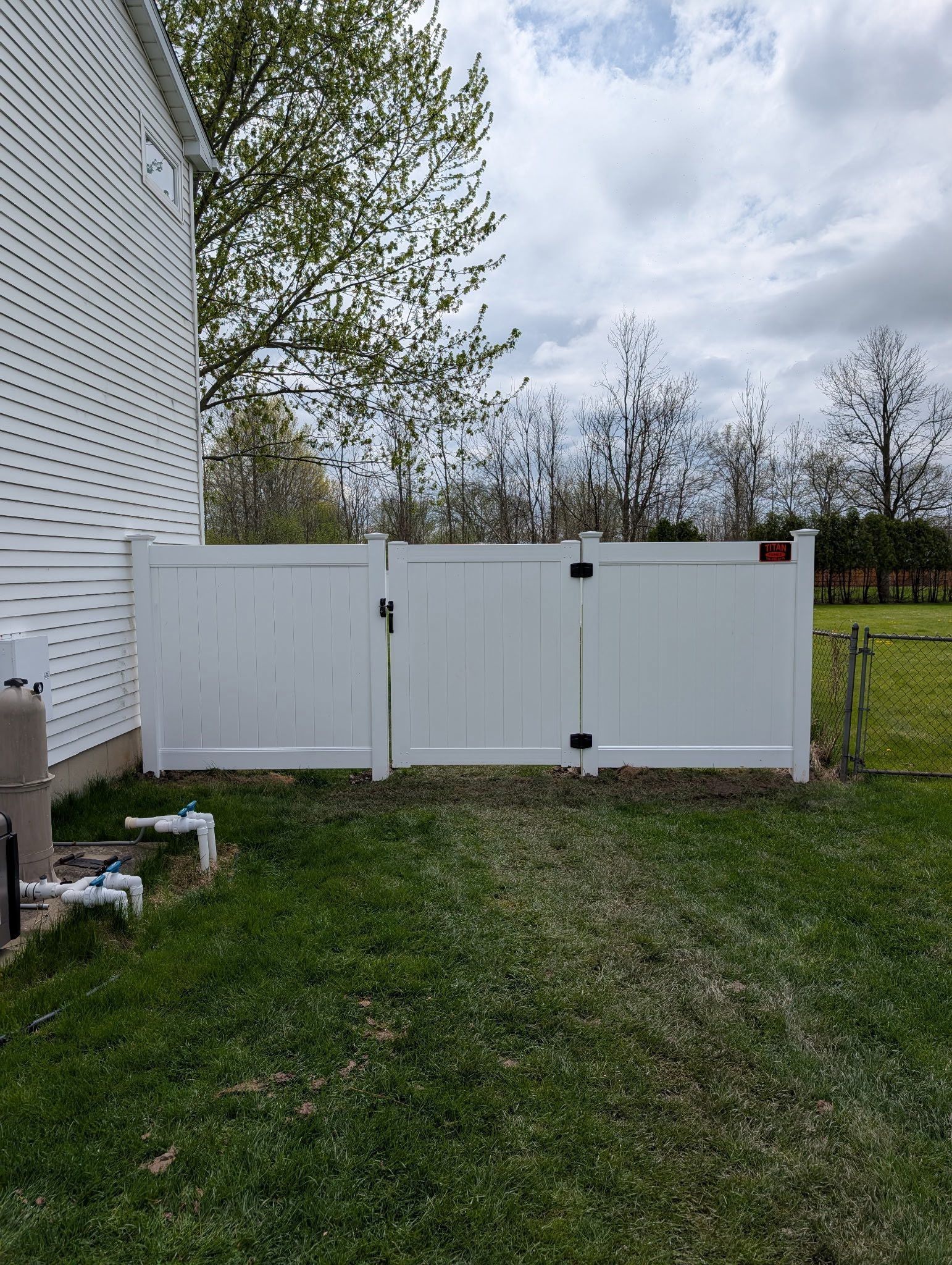 White outdoor storage unit beside a house, set in a grassy yard under a cloudy sky.