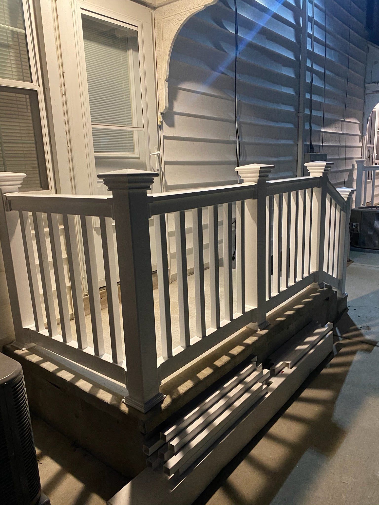 Porch with white railing and steps beside a house at night
