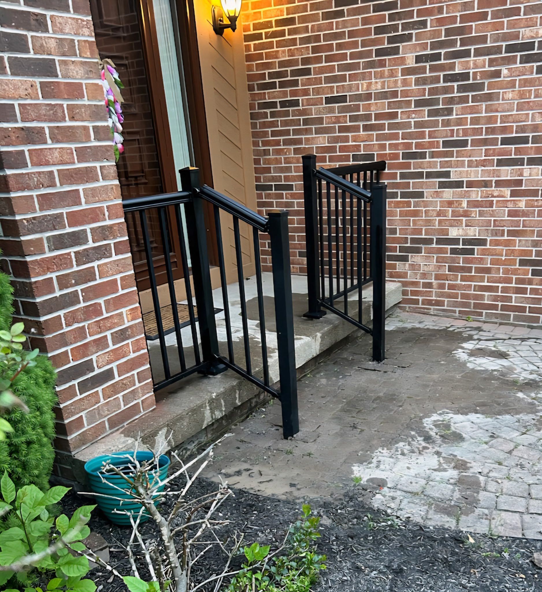 Brick apartment entrance with black railings and concrete steps under a wall light.