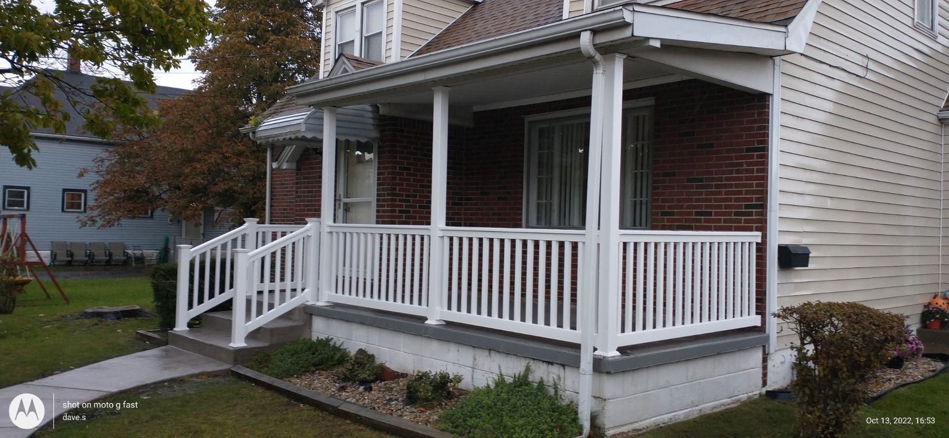 Front porch with white railing and steps on a brick house in a leafy neighborhood