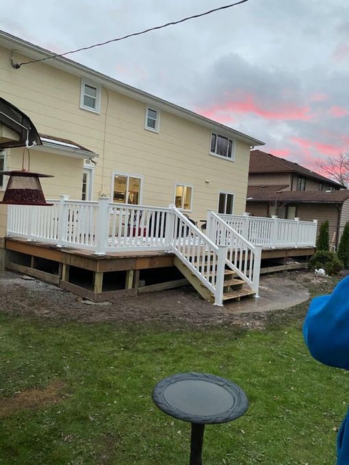 Backyard deck with white railings and stairs beside a beige house at dusk