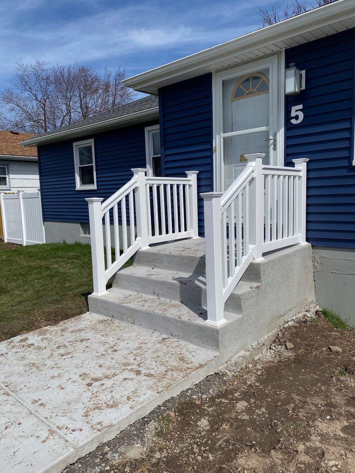 Blue house entrance with concrete steps, white railings, and a white door numbered 5