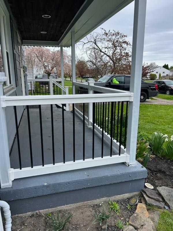 Front porch with black railings, gray steps, and a view of a suburban street and parked cars