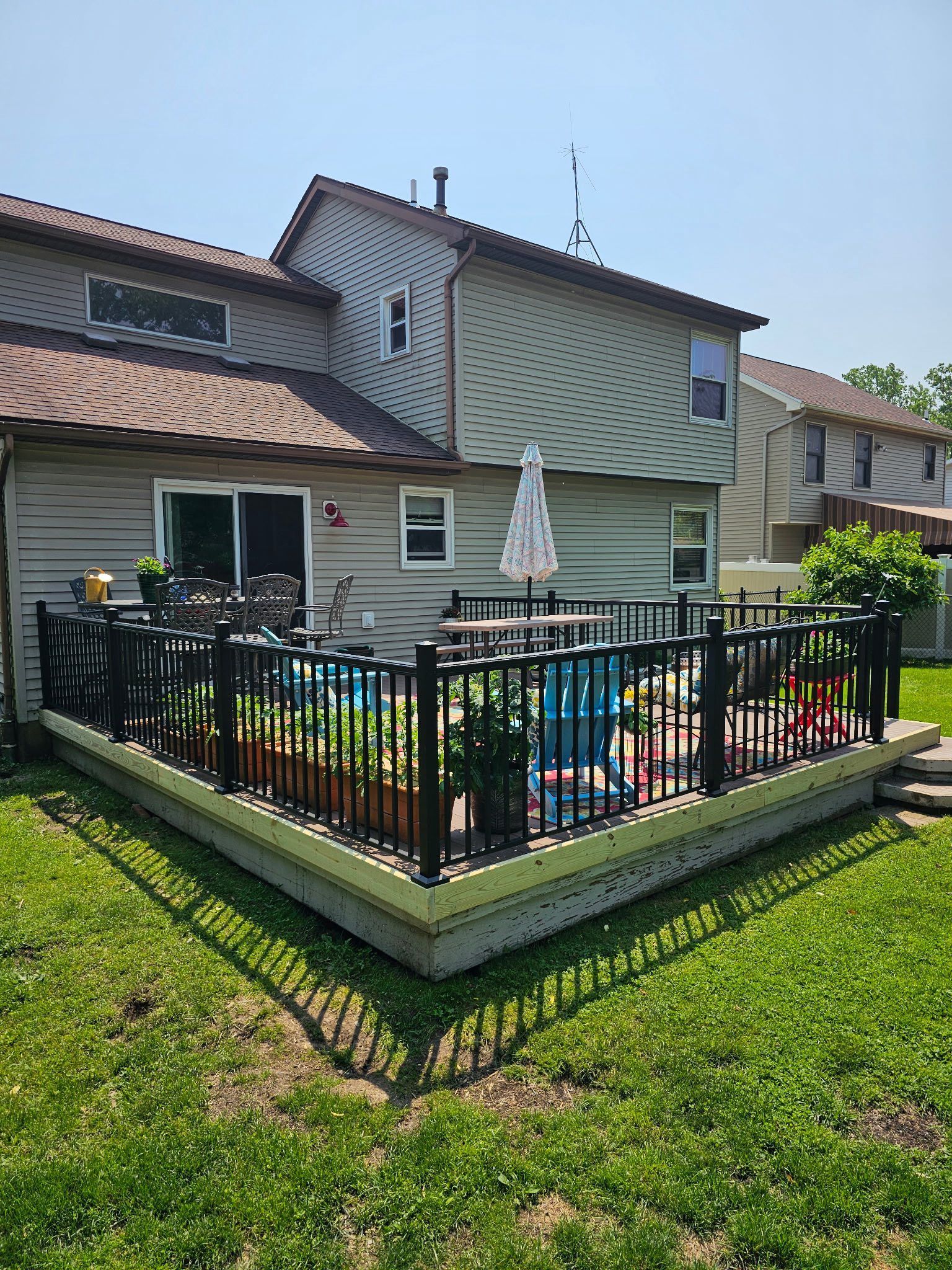 Backyard patio with black railing, umbrella, potted plants, and a small above-ground pool beside a house