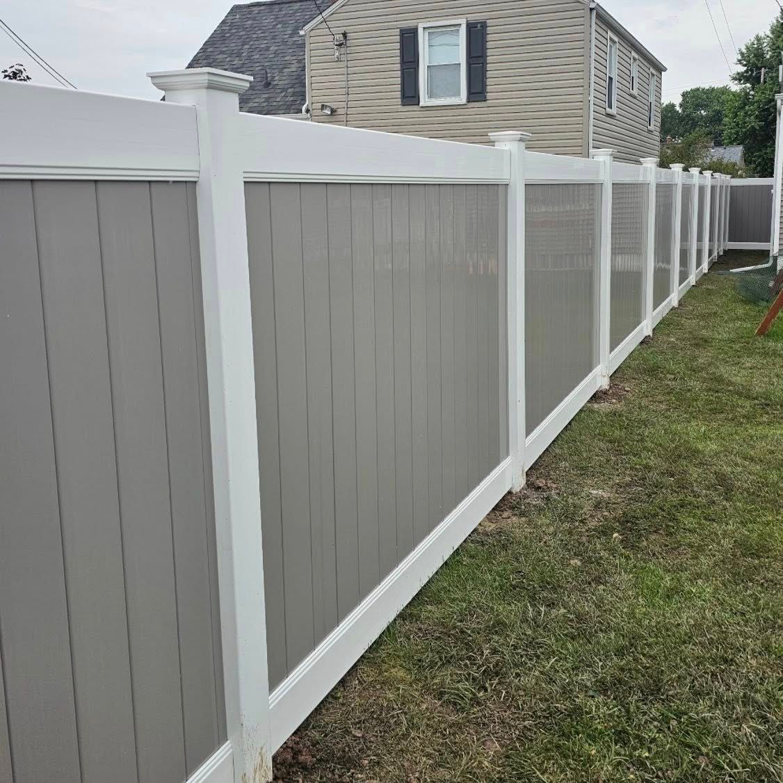 White and gray vinyl fence along a grassy yard beside a house