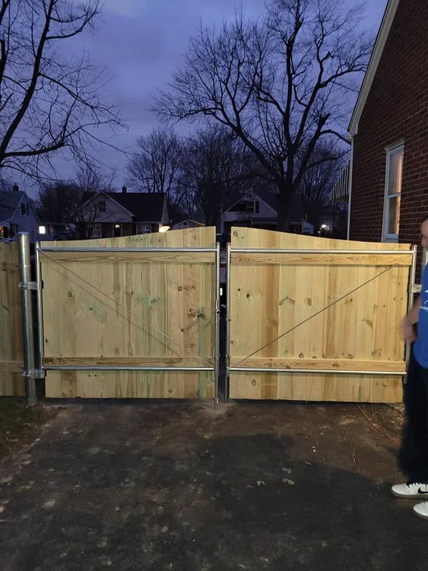Wooden double gate at the end of a driveway at dusk, with bare trees and houses in the background.
