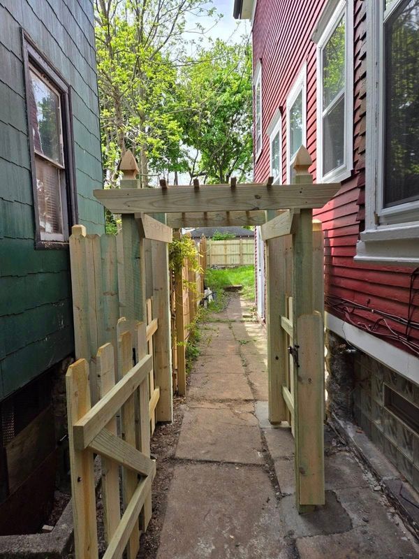 Narrow stone path between red and green houses, with a wooden gate and arbor overhead.