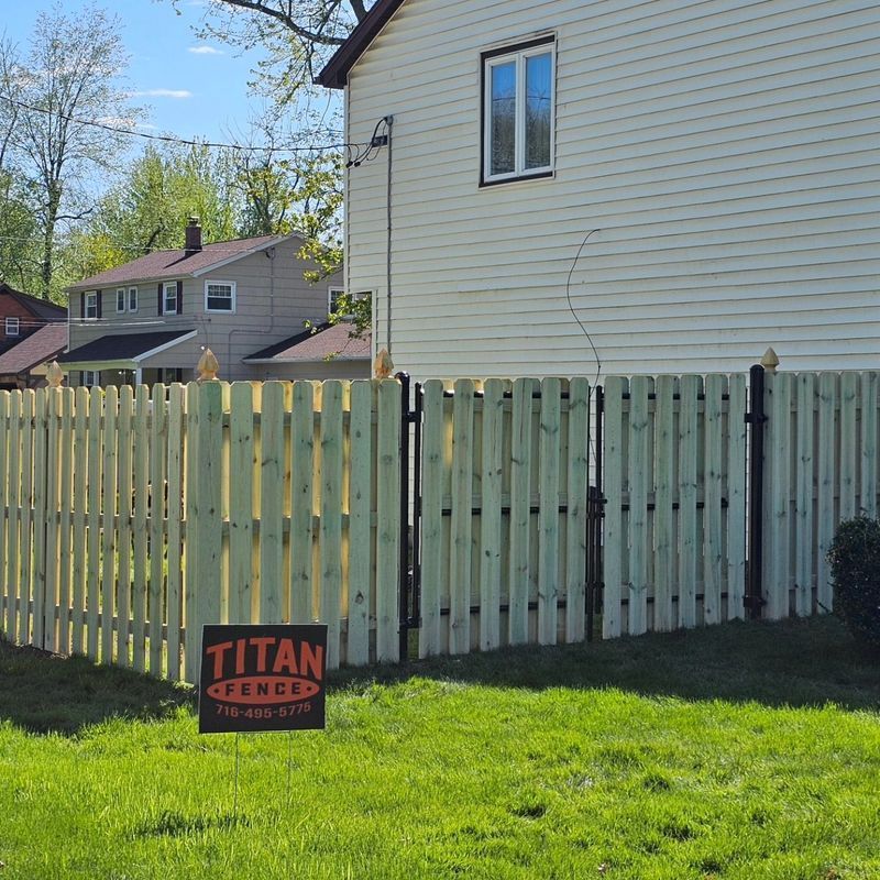 Backyard with pale wooden fence, green lawn, beige house, and a Titan Fence sign in front