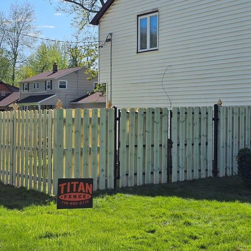 Backyard with pale wooden fence, green lawn, beige house, and a Titan Fence sign in front