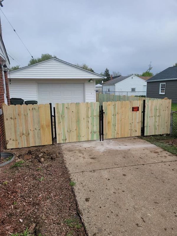 Wooden gate blocking a driveway, with a garage and houses visible behind it.