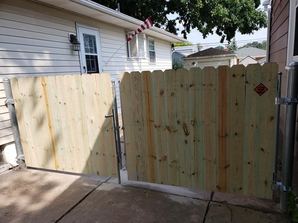 Wooden backyard gate between fences, with a side yard and house visible behind it.