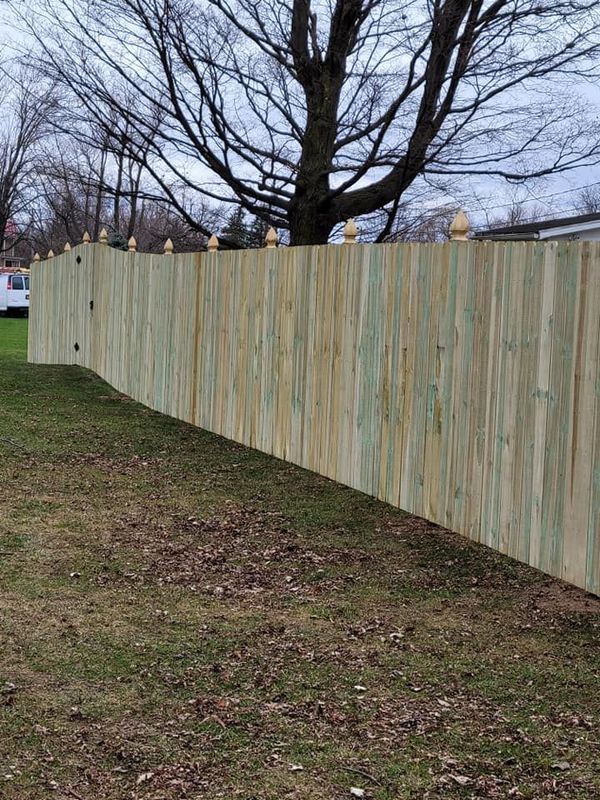 Tall wooden fence beside a grassy field with leafless trees in the background