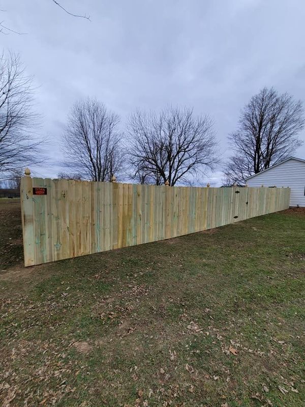Freshly built wooden privacy fence along a grassy yard under an overcast sky