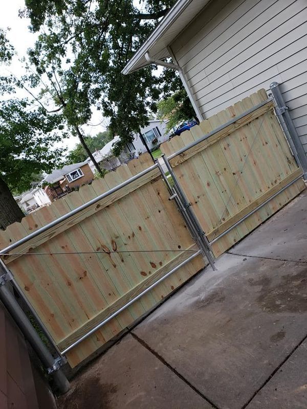 Wooden driveway gate beside a concrete driveway, with trees and a house in the background.