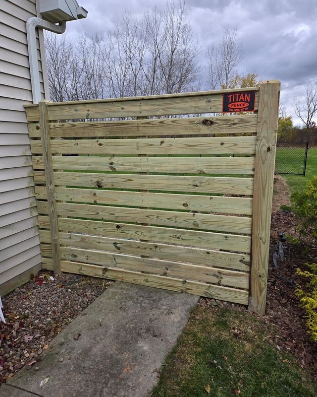 Wooden privacy gate beside a house, with a concrete path leading up to it.