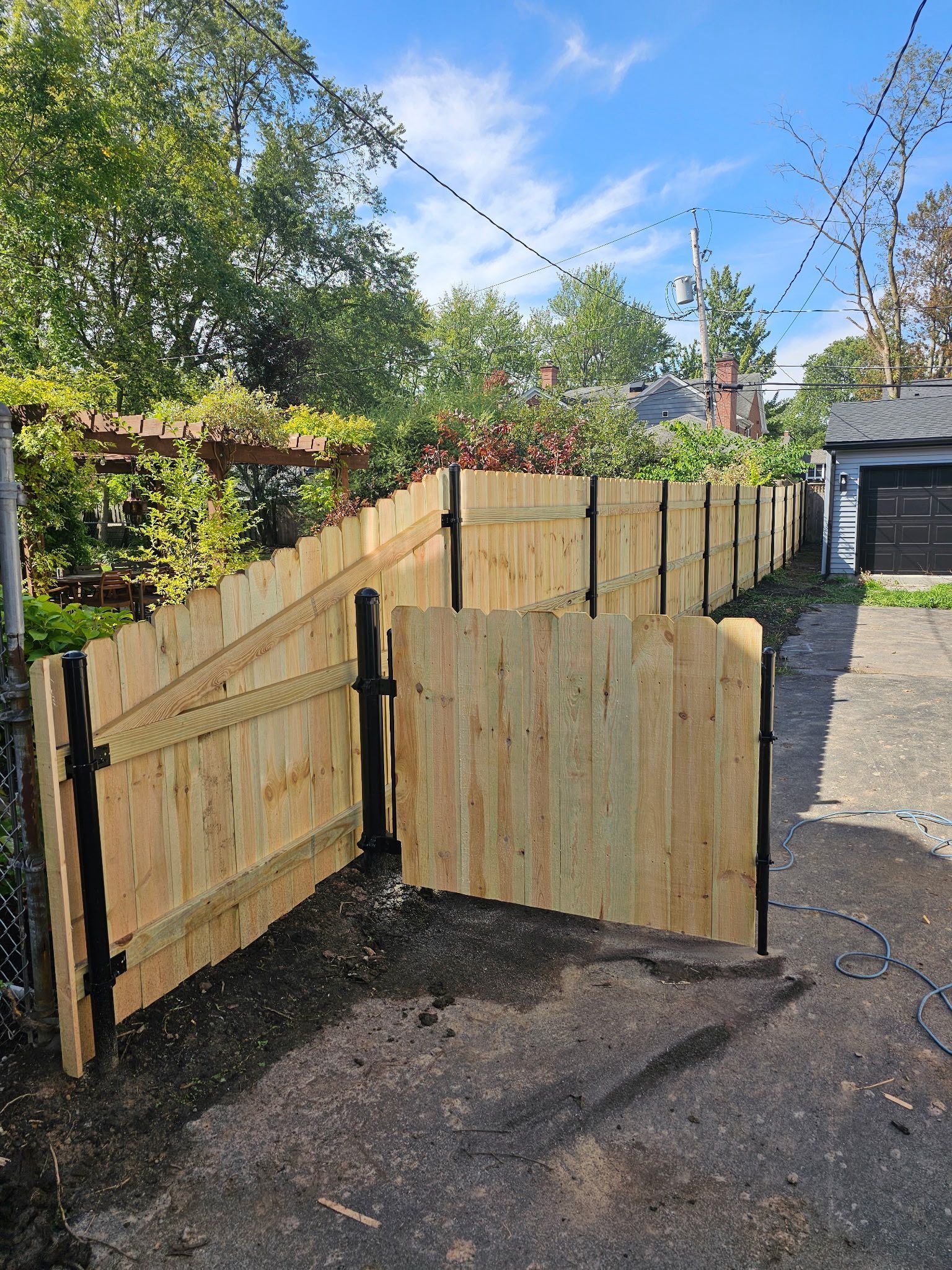 Wooden garden fence and gate beside a paved driveway under a blue sky