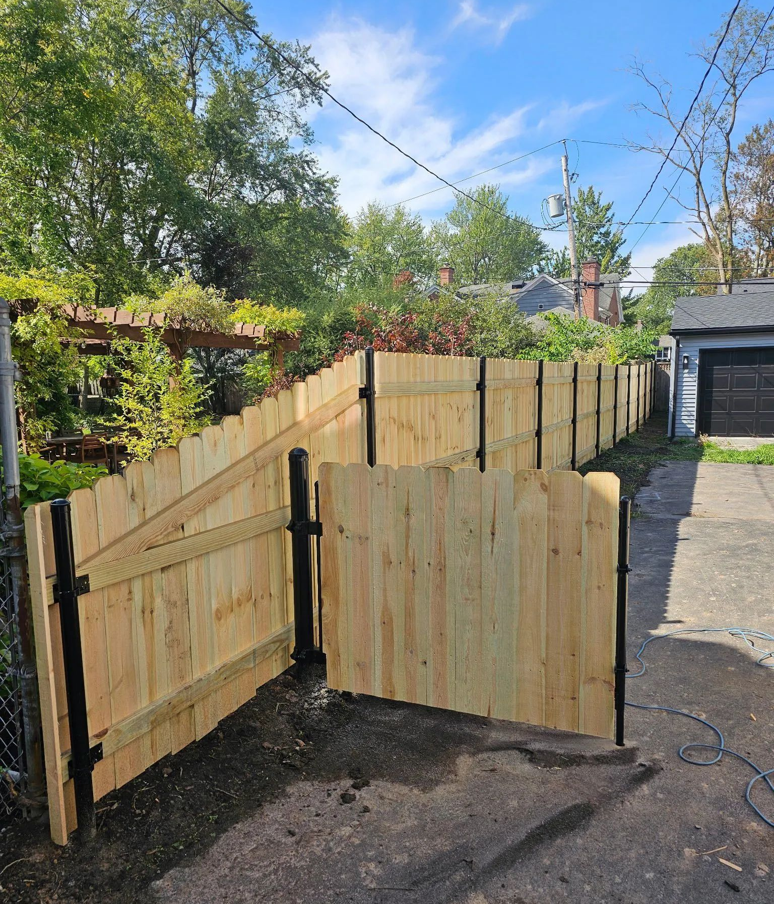 Wooden gate panels blocking a driveway beside a fence, with a garage and trees in the background