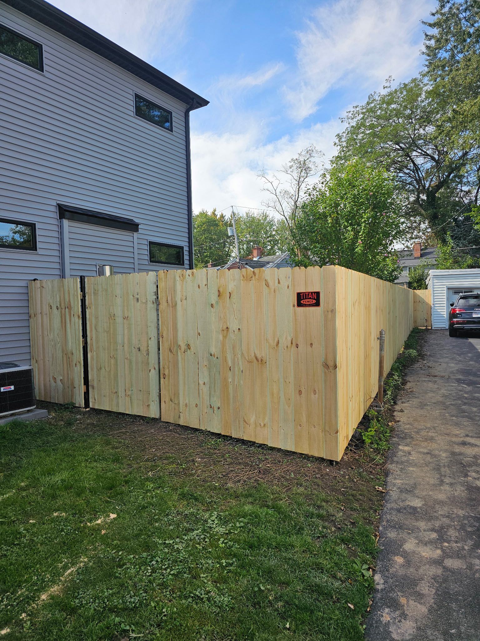 Large wooden enclosure beside a house, with a driveway and trees in the background.