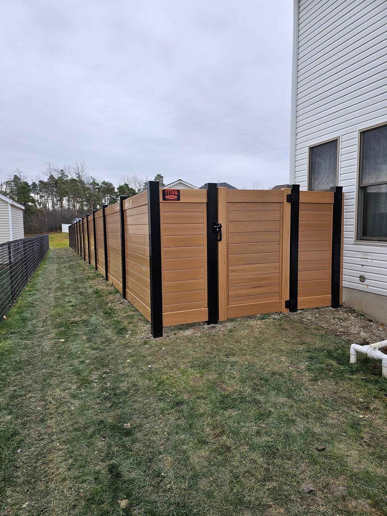 White vinyl fence and gate along a gravel path beside tall green trees under a blue sky