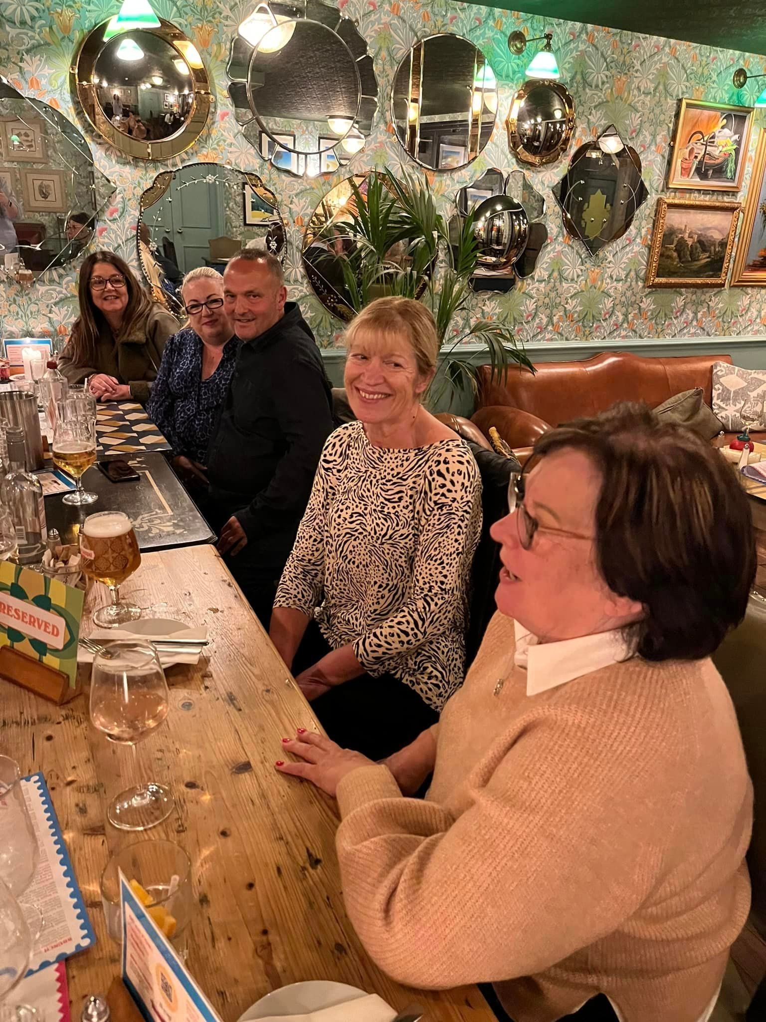 People sitting at a wooden table in a restaurant with a patterned wallpaper and decorative mirrors on the wall.