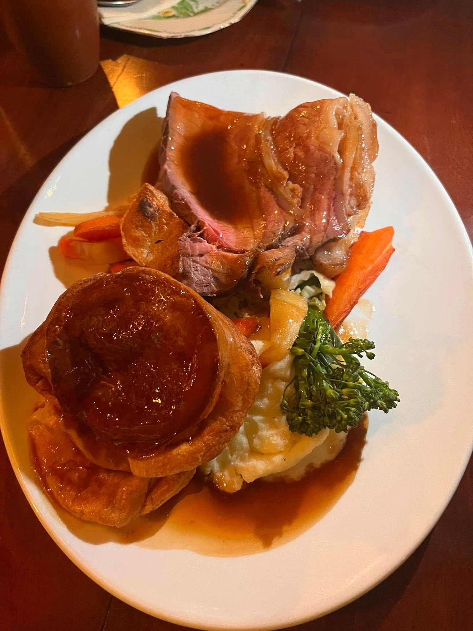 A Sunday roast dinner with slices of beef, gravy, a Yorkshire pudding, roasted vegetables, and mashed potatoes.