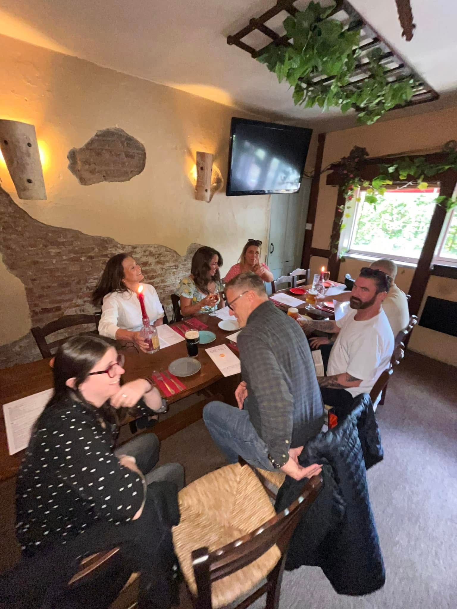 A group of people sit around a wooden table in a rustic restaurant for a social meal.