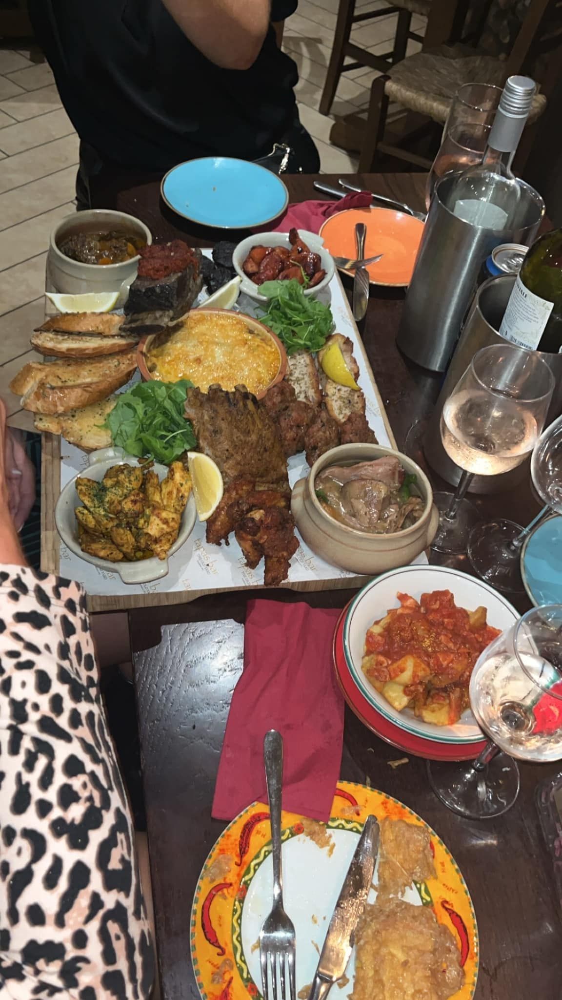A large wooden board filled with assorted appetizers, fried foods, and small bowls of dips on a table set for dinner.