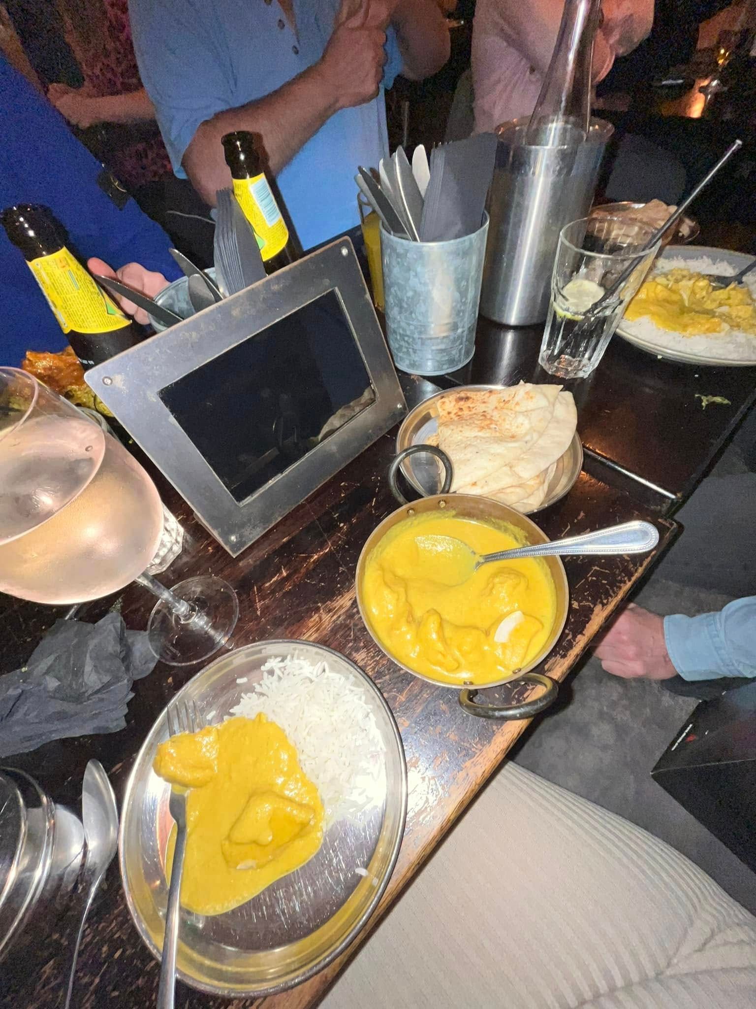 A dining table with bowls of yellow curry, white rice, naan bread, and drinks, viewed from an overhead perspective.
