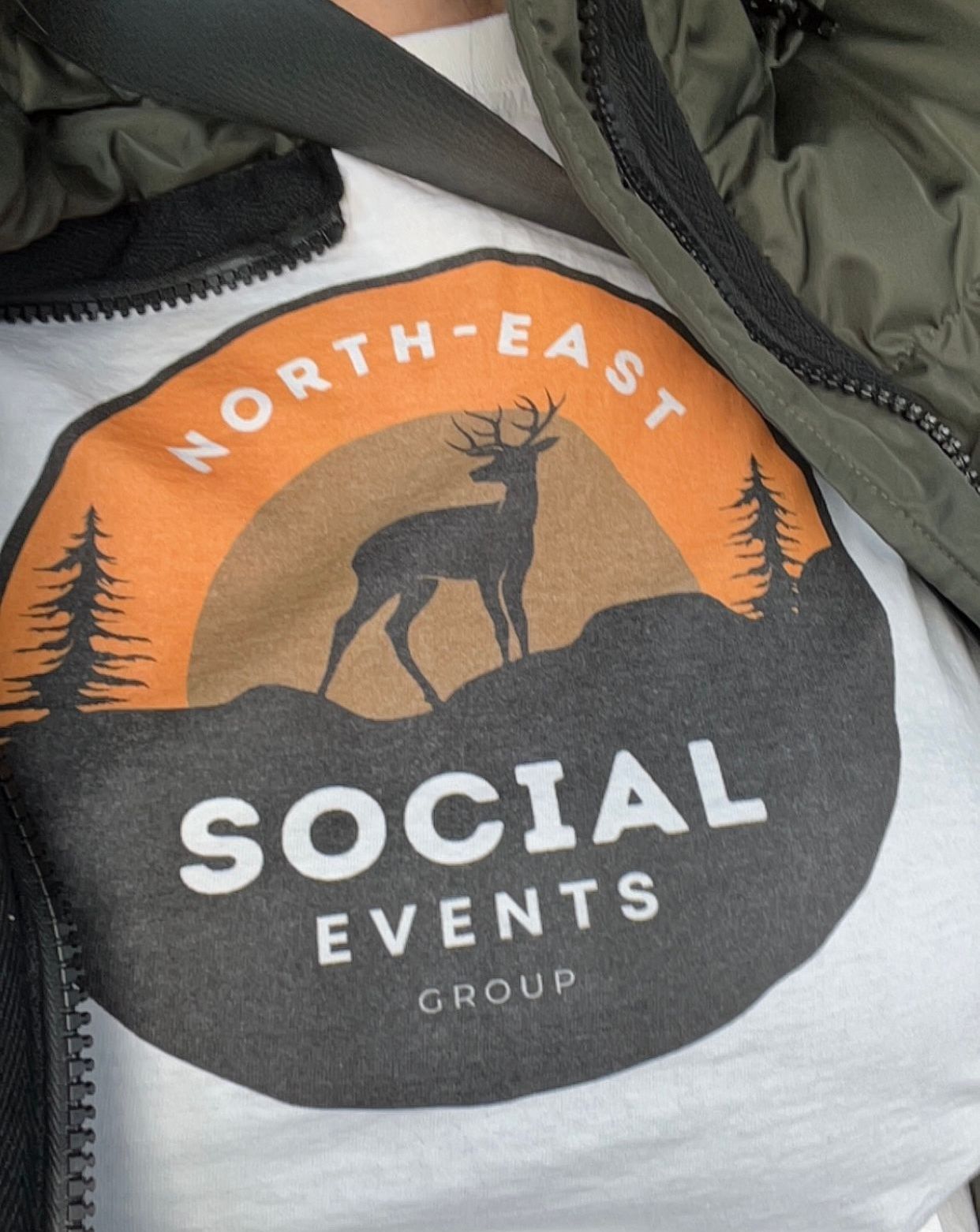 A logo for North-East Social Events Group featuring an orange sunset, a silhouette of a deer, and pine trees.