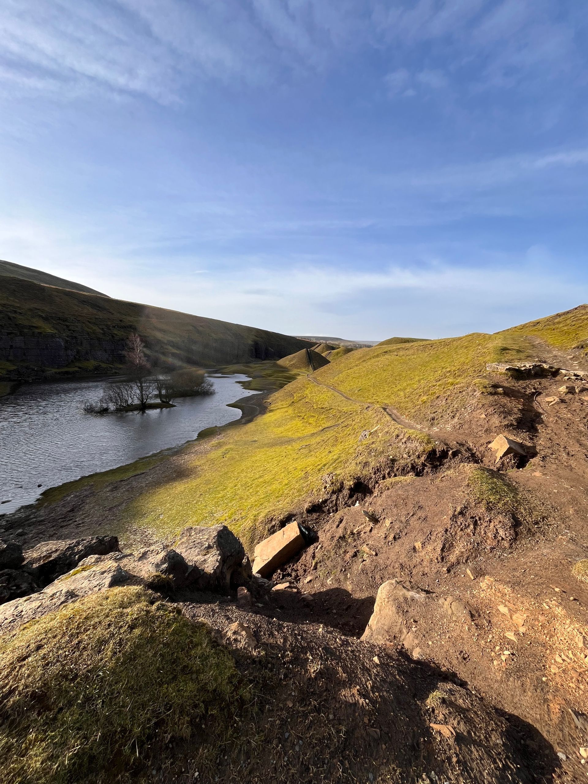 A stream winds through a green, rocky valley under a bright blue sky.