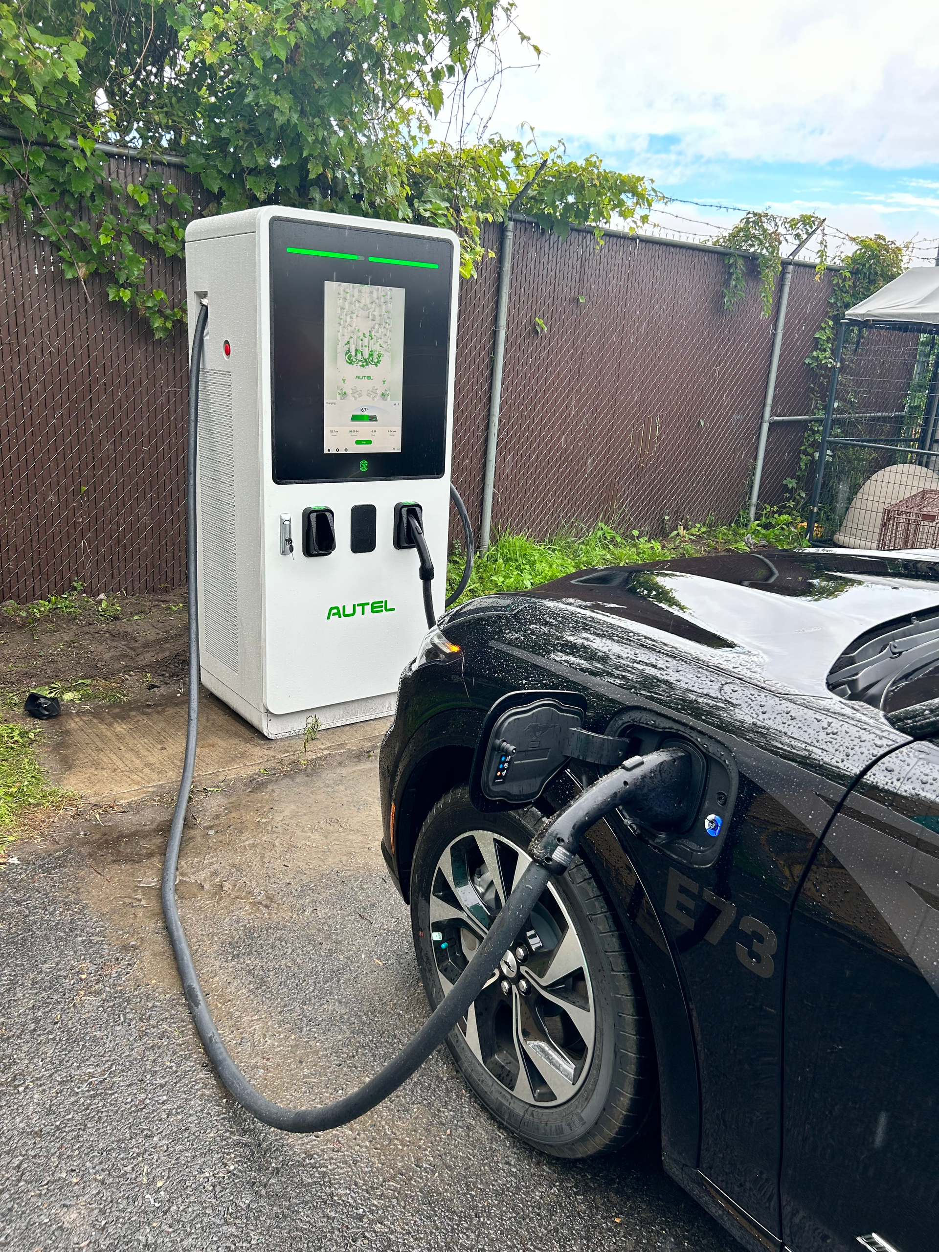 Une voiture noire se recharge sur une borne de recharge pour véhicule électrique blanche à l'extérieur.