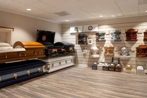 Funeral caskets displayed in a showroom with wood floors and bright ceiling lights