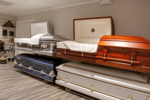 Display room with three caskets in silver, blue, and wood finishes on display shelves