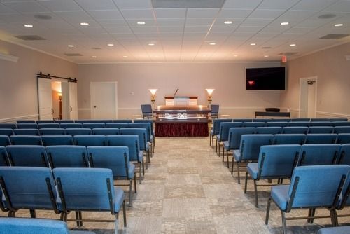 Empty chapel seating facing an altar, with rows of blue chairs in a softly lit room