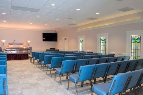 Blue chairs arranged in rows inside a small chapel or funeral home with an altar at the front
