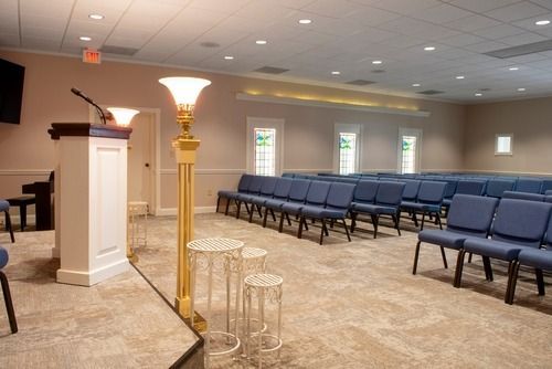 Empty church-like auditorium with blue chairs, a podium, and a lit floor lamp on carpeted floor