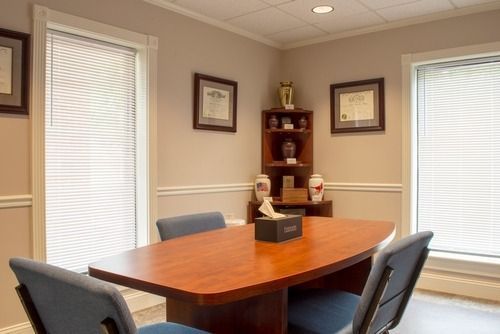 Conference room with wooden table, blue chairs, framed art, and a corner shelf with decor.