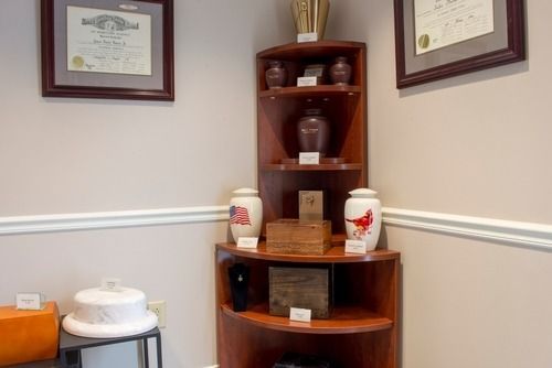 Wall-mounted certificates above a corner display cabinet with urns, vases, and small plaques in a room